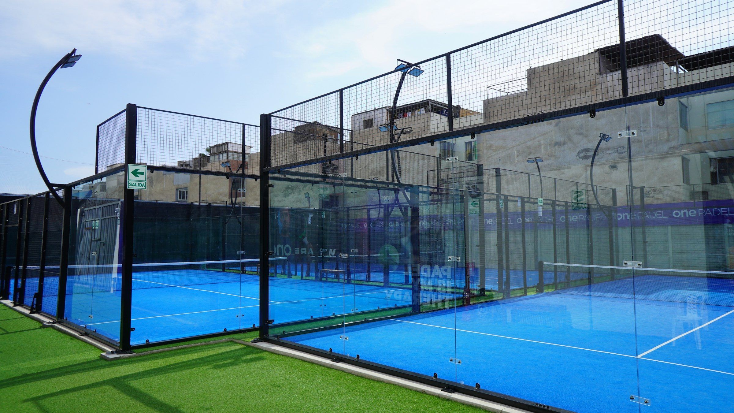 Outdoor-Padelcourt mit Glaswänden und blauem Kunstrasen unter blauem Himmel