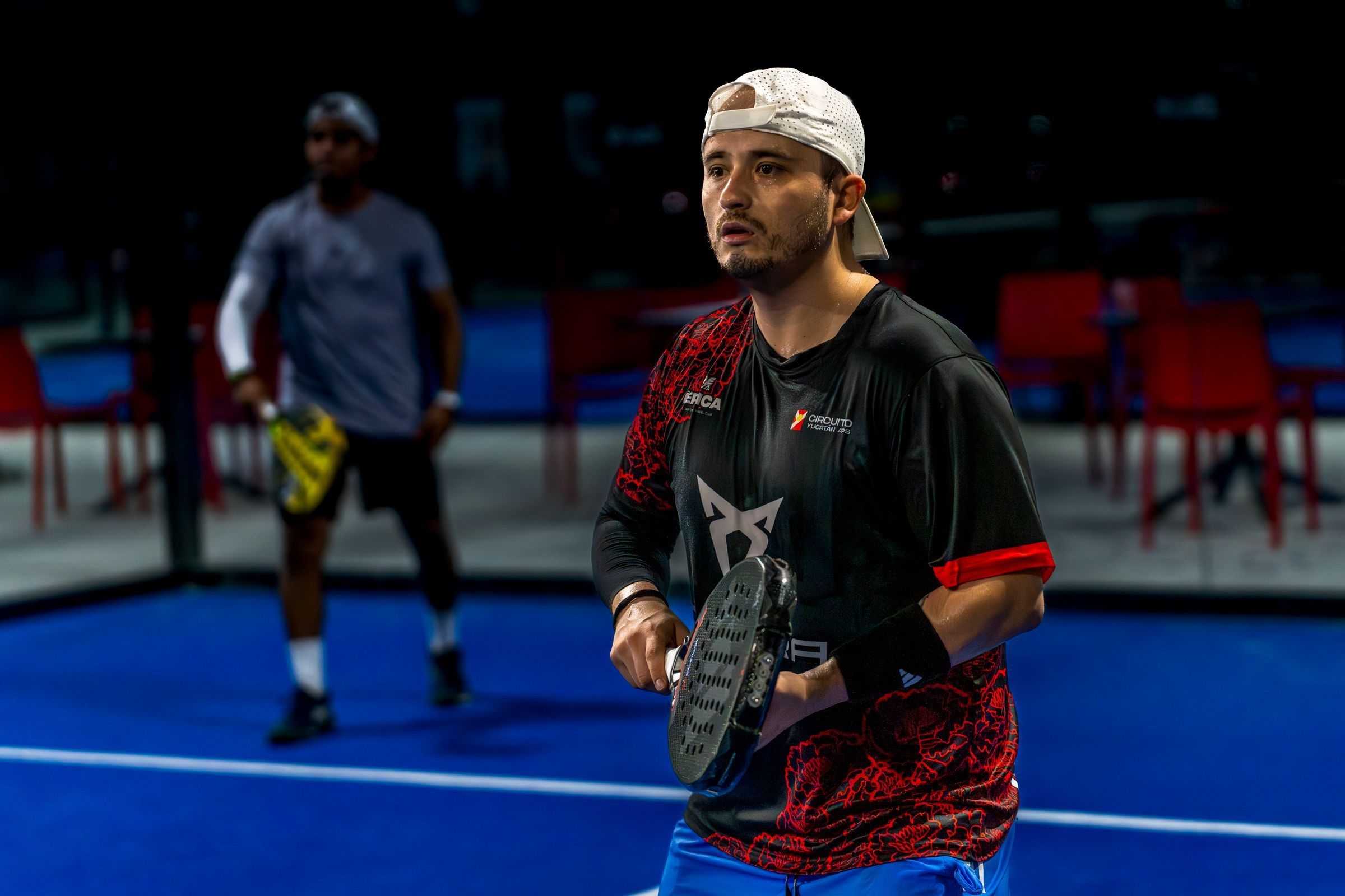 Zwei Padelspieler stehen auf einem blauen Indoor-Court bereit für den nächsten Ball