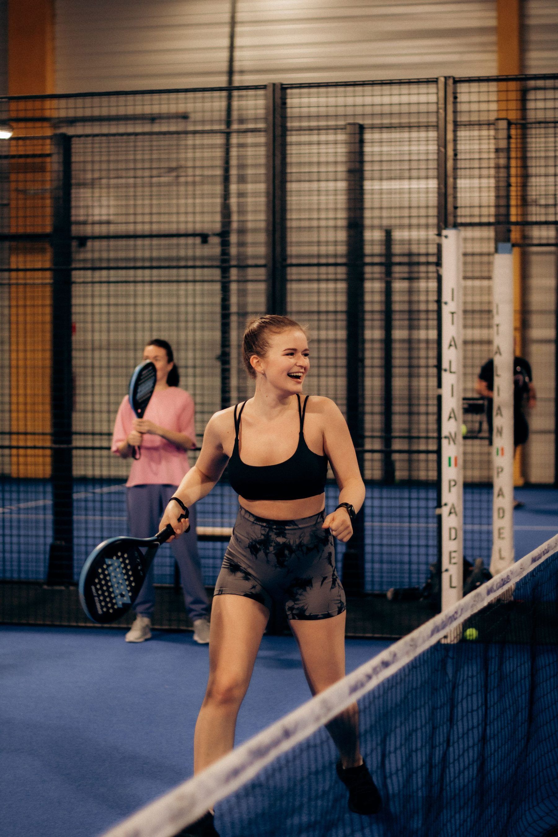 Zwei Padelspielerinnen stehen nebeneinander auf einem Indoor-Court und erwarten den Ball