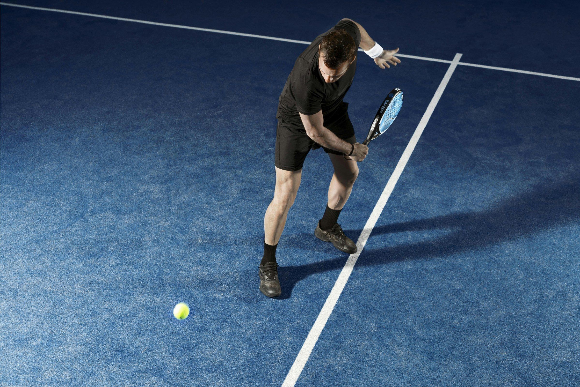 Padelspieler spielt eine tiefe Vorhand auf einem dunkelblauen Court, der Ball liegt vor ihm