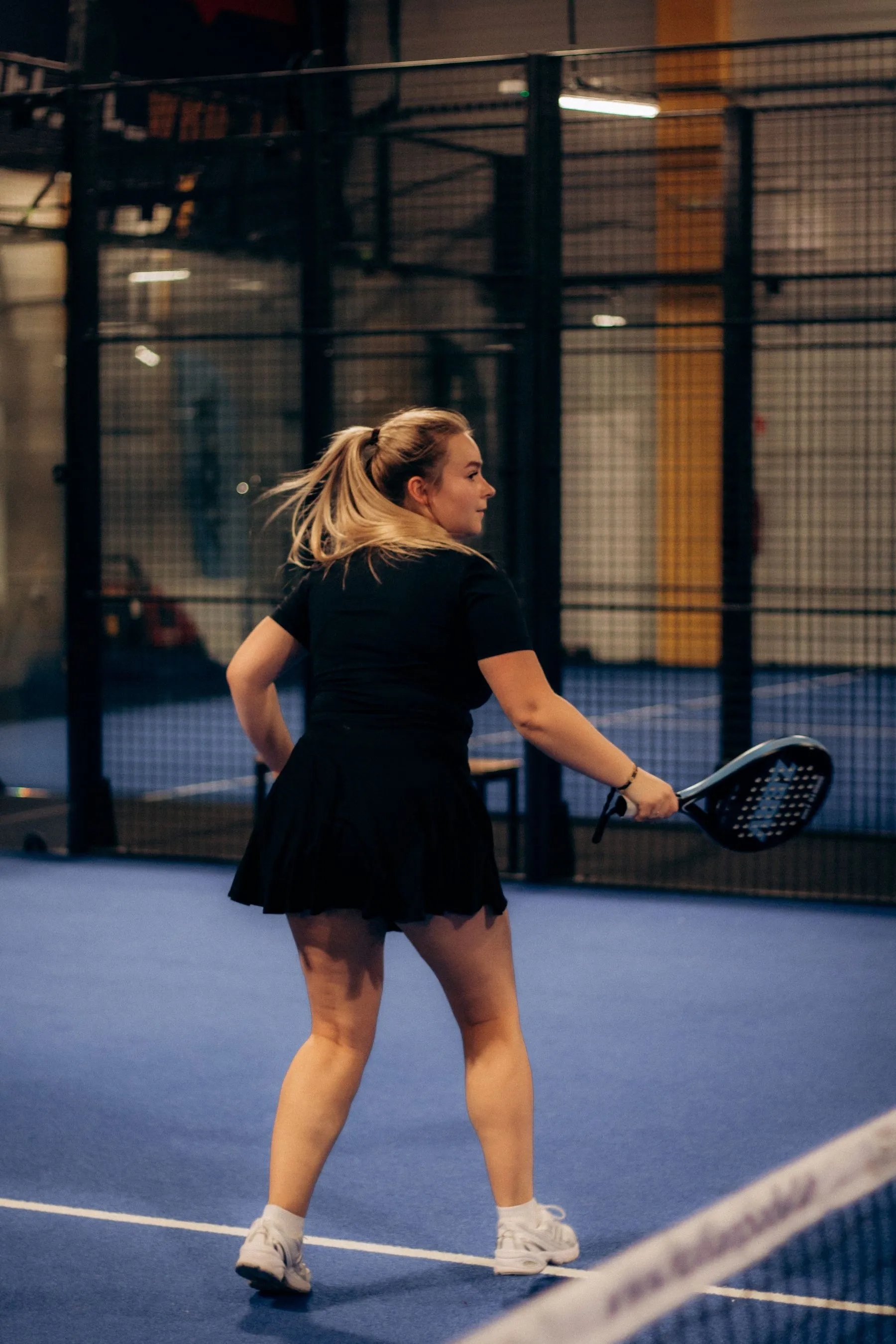 Padelspielerin holt auf einem blauen Indoor-Court zur Vorhand aus