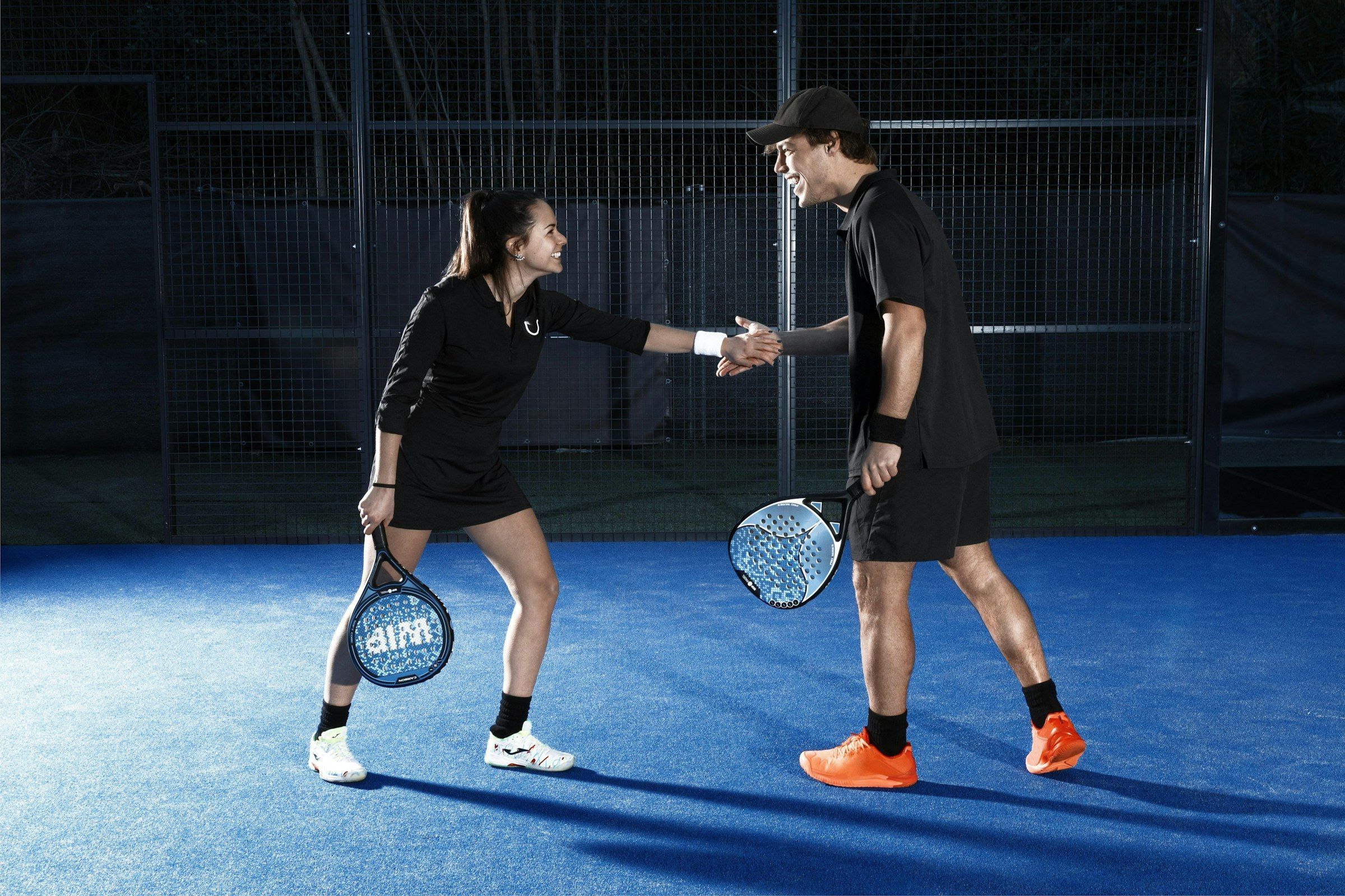 Padelspielerin und Padelspieler geben sich auf einem dunkelblauen Court die Hand