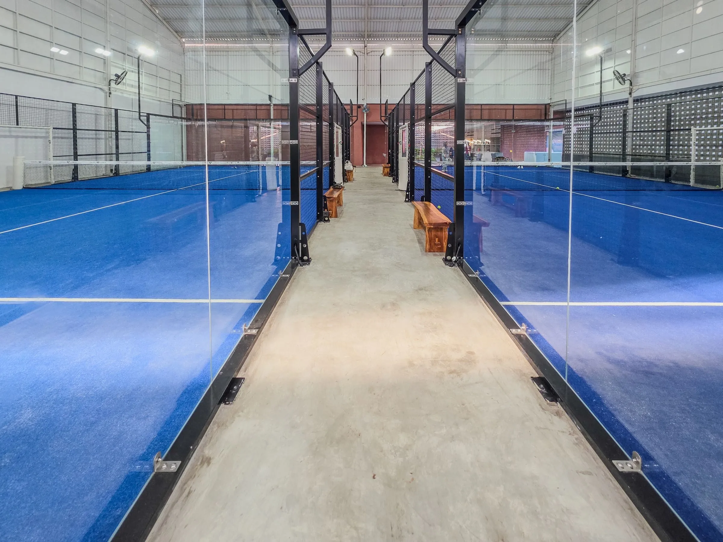 Moderne Padelhalle mit mehreren blauen Courts und Glaswänden unter einem hohen Dach