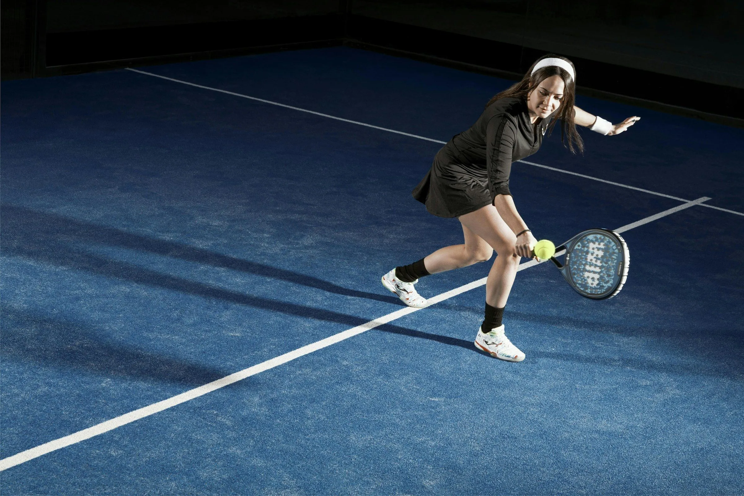 Padelspielerin geht für einen tiefen Ball in die Knie, der Schläger ist unter dem Ball