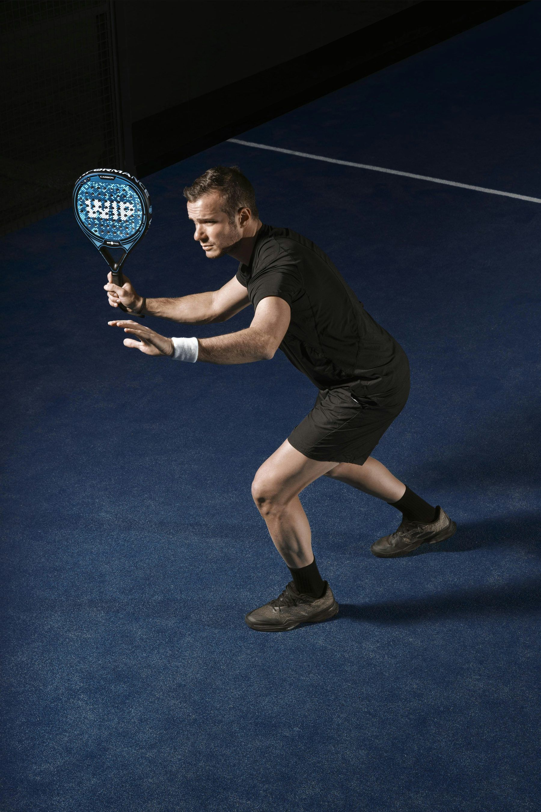 Padelspieler in tiefer Bereitschaftsstellung mit dem Schläger vor dem Körper auf einem dunkelblauen Court