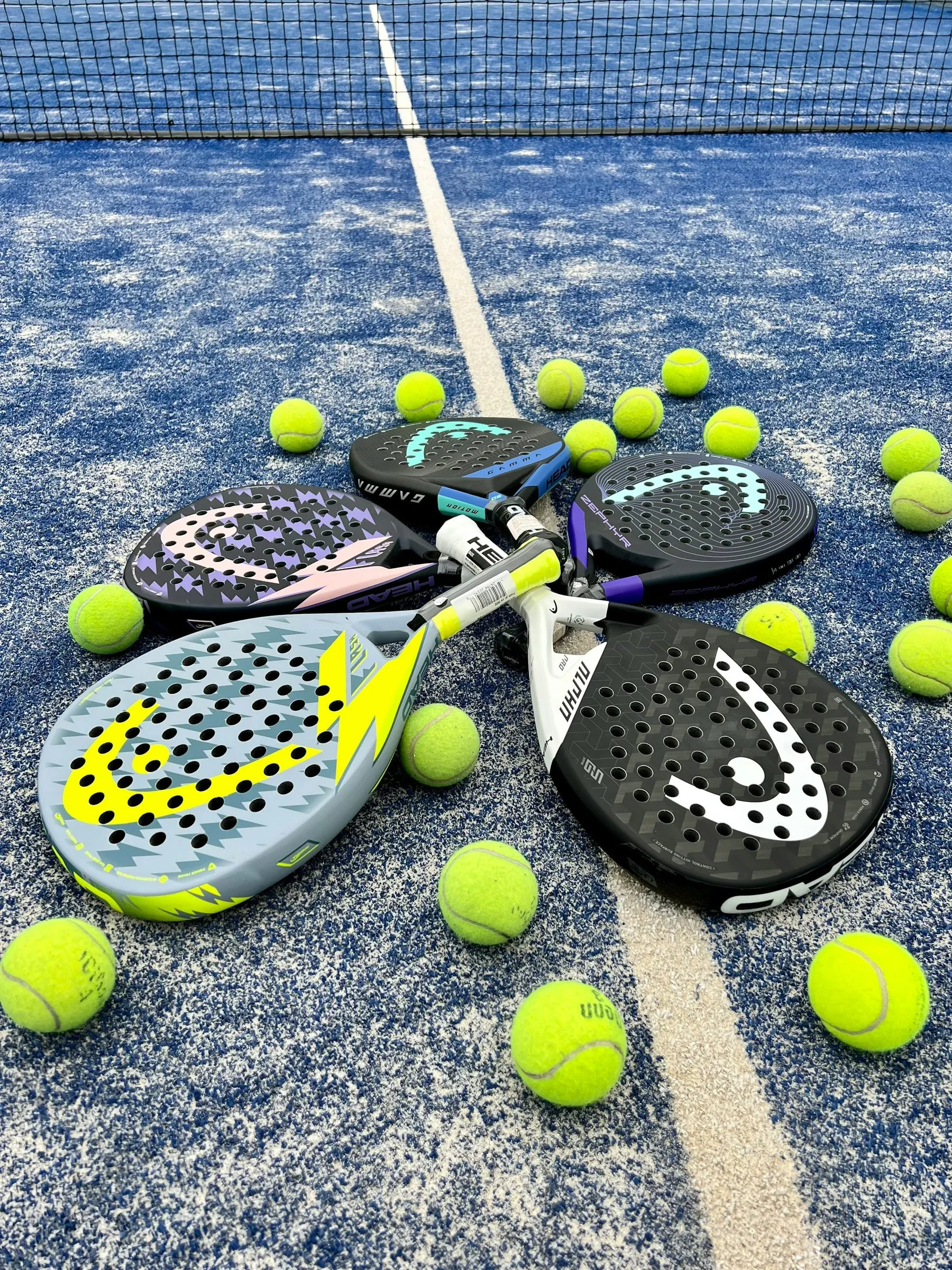 Vier Padelschläger liegen im Kreis mit gelben Bällen auf einem blauen Court