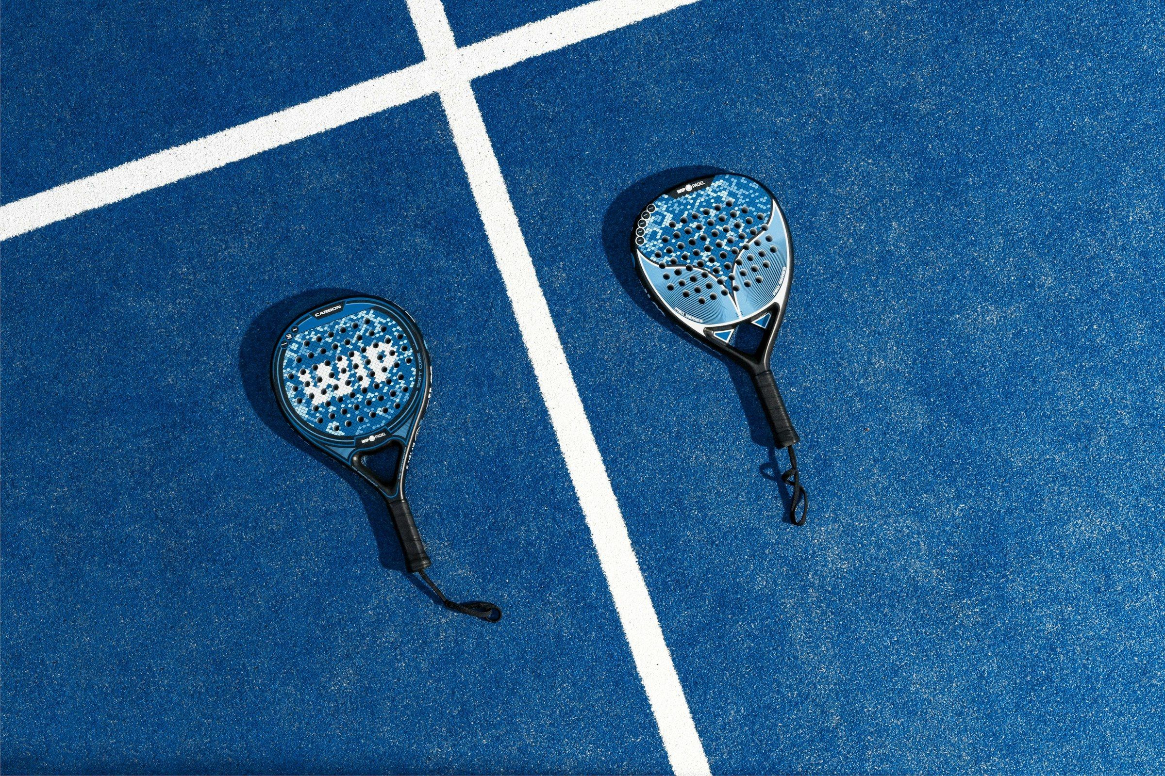 Zwei Padelschläger liegen nebeneinander auf einem blauen Court mit weißen Linien