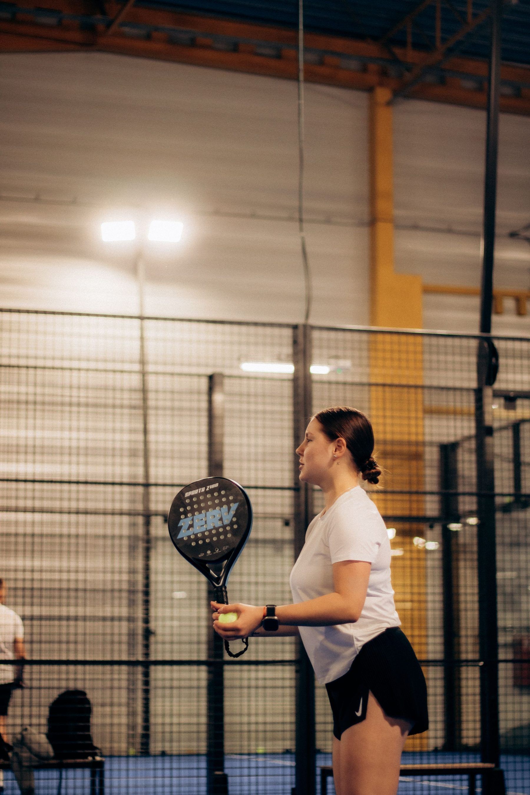 Padelspielerin bereitet sich auf einem Indoor-Court auf den Aufschlag vor, Ball in der Hand